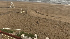 A beach with a clear sky, waves, and a sandy area with a white structure. - Sea Beach House (Oliva)