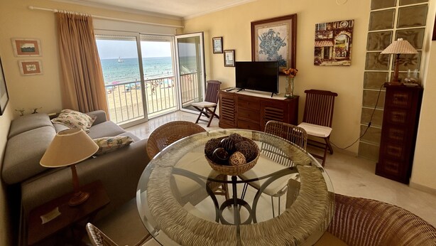 A living room with a glass table, a sofa, a TV, and a view of the beach. - Sea Beach House (Oliva)