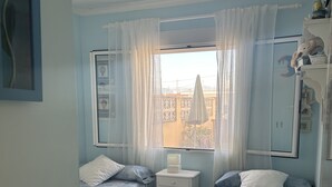 A bedroom with two beds, a nightstand, a crib, and a window with curtains. - Sea Beach House (Oliva)
