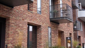Un edificio de varios pisos de ladrillo con balcones, ventanas amplias y macetas a lo largo de la acera.
