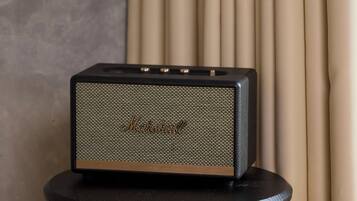 A Marshalls speaker on a small table against a backdrop of beige curtains and a textured wall.