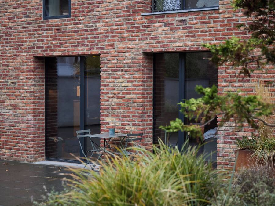 Ein modernes Backsteingebäude mit großen Fenstern und einer Terrasse mit Gartenmöbeln.