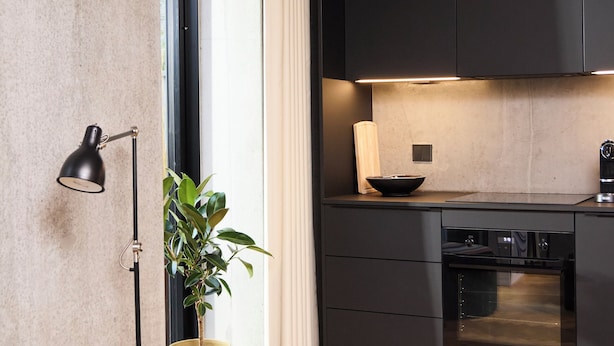 Una cocina moderna con armarios oscuros, horno empotrado y una planta en maceta.
