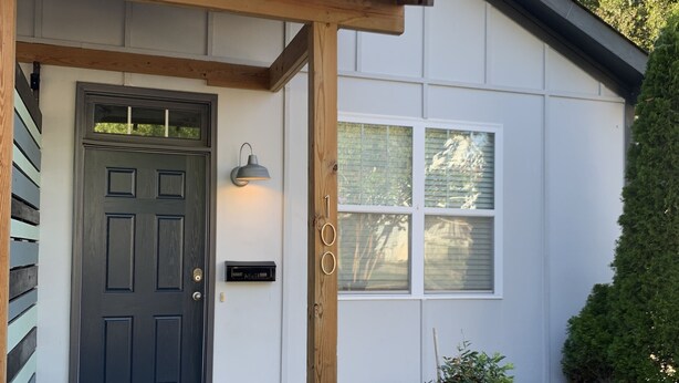 Une maison avec une porte d’entrée sombre, un porche en bois, une boîte aux lettres et un pot de fleurs.
