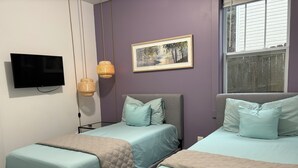 Une chambre avec deux lits, une télévision, un tableau et une fenêtre.