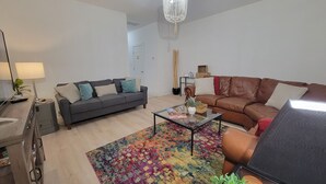 Un salon moderne avec un canapé gris, un canapé en cuir marron, une table basse en verre et un tapis coloré.
