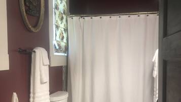 A bathroom with a toilet, a sink, a mirror, a towel rack, and a window with floral curtains.