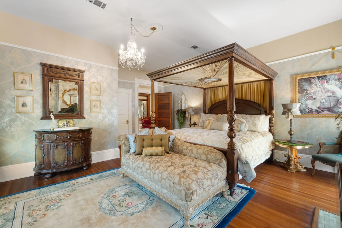 Une chambre spacieuse avec un lit à baldaquin, une commode en bois et un lustre.