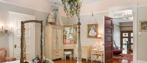 A bedroom with a four-poster bed, a dresser, a vanity, and a chandelier.