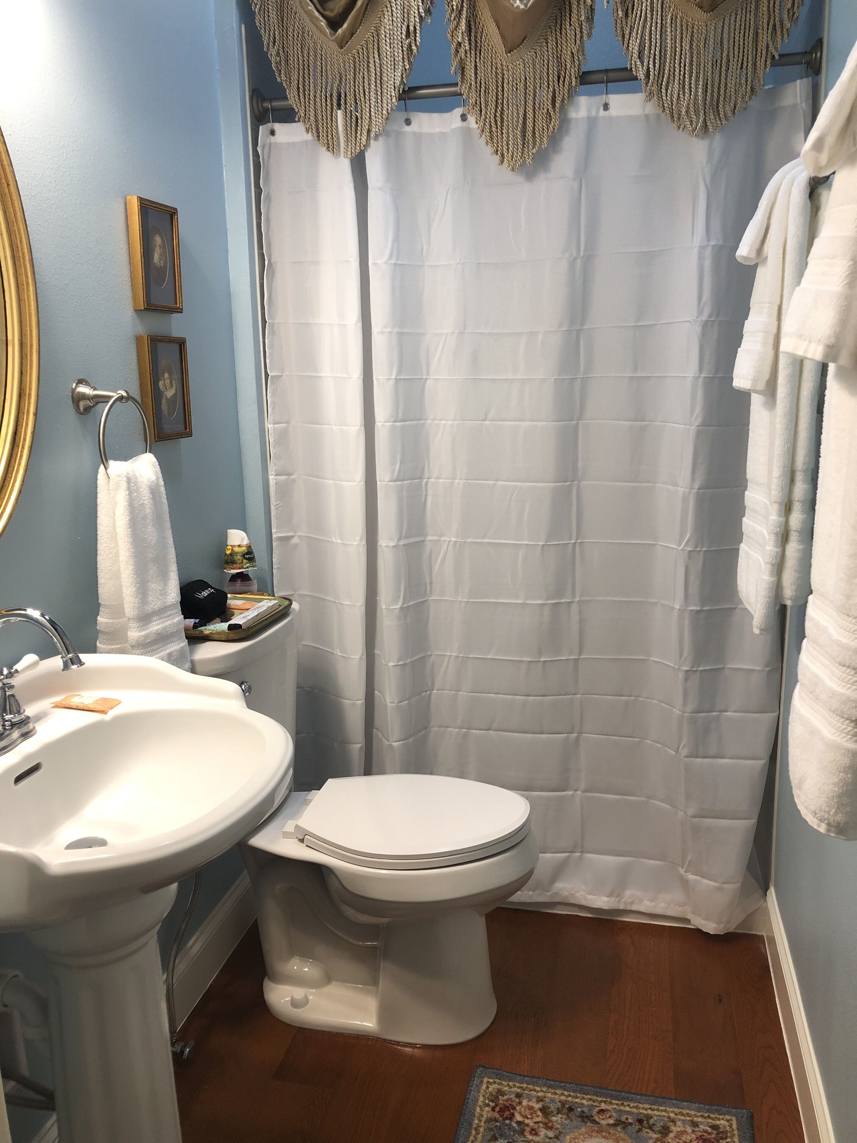 A bathroom with a white sink, toilet, and shower curtain. There are framed pictures on the wall and a towel rack.