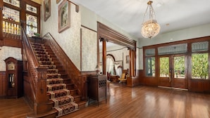 Un magnifique escalier orné de boiseries sculptées, un lustre et de grandes fenêtres avec des vitraux.