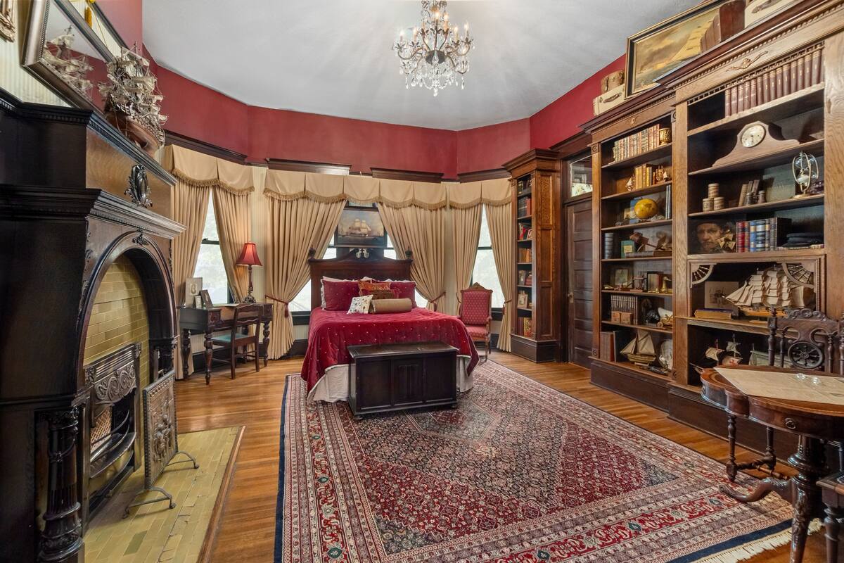 Une pièce dotée d’un grand lit, d’une cheminée, d’une bibliothèque et d’un lustre.