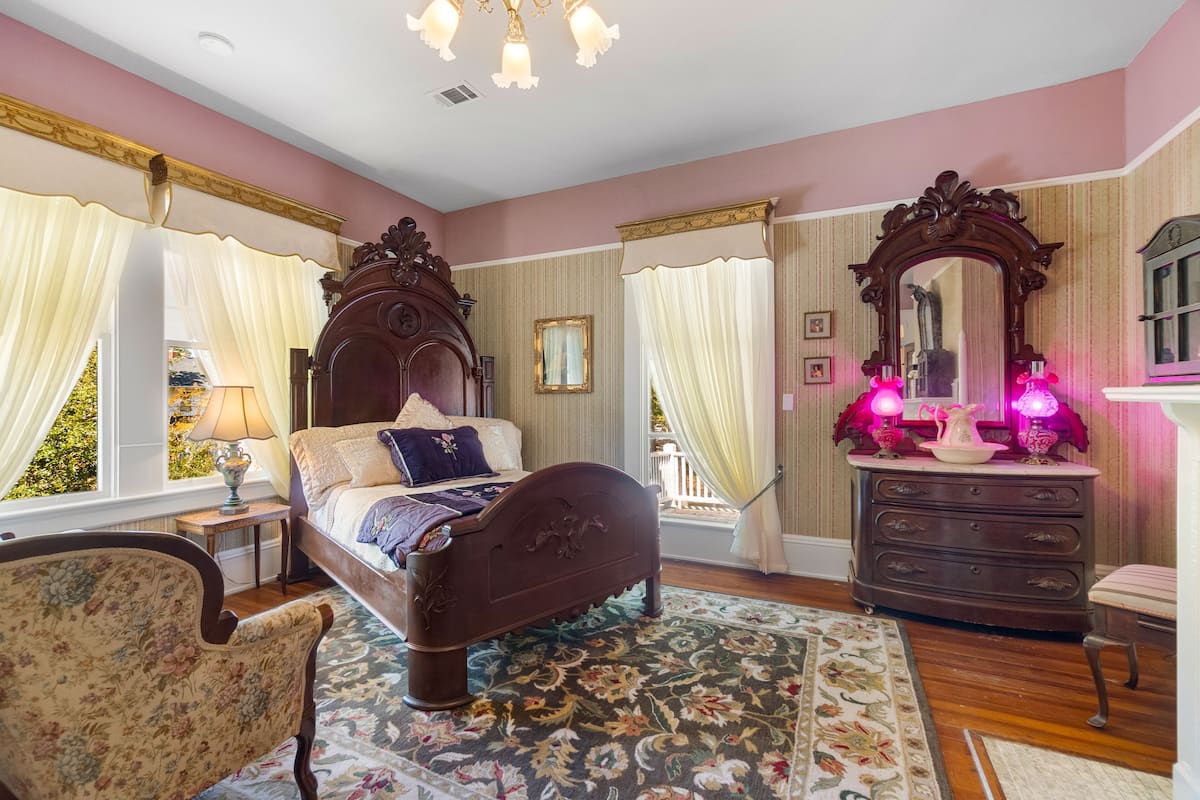 Une chambre à coucher avec un lit à baldaquin, une commode, une chaise et un grand miroir.