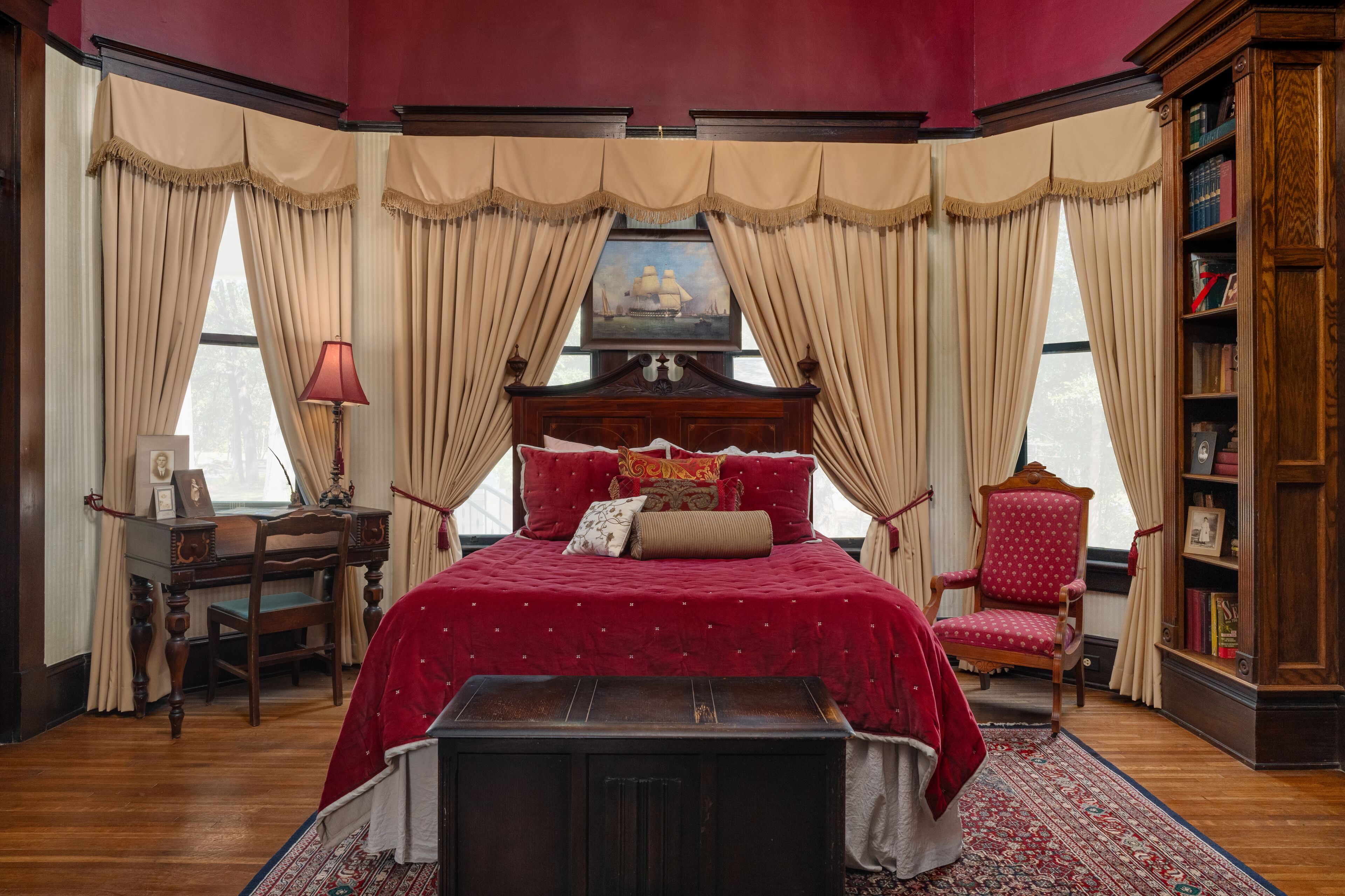 Een slaapkamer met een groot bed, een houten bureau, een stoel en een boekenkast.