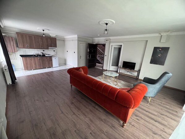 A modern living room with a red sofa, a grey armchair, a small round coffee table, and a TV on a stand. - Konak Suite Ankara (Ankara)