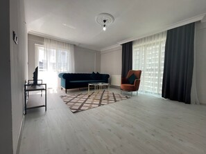 A spacious living room with a dark blue sofa, a brown armchair, a coffee table, and a TV on a stand. - Konak Suite Ankara (Ankara)