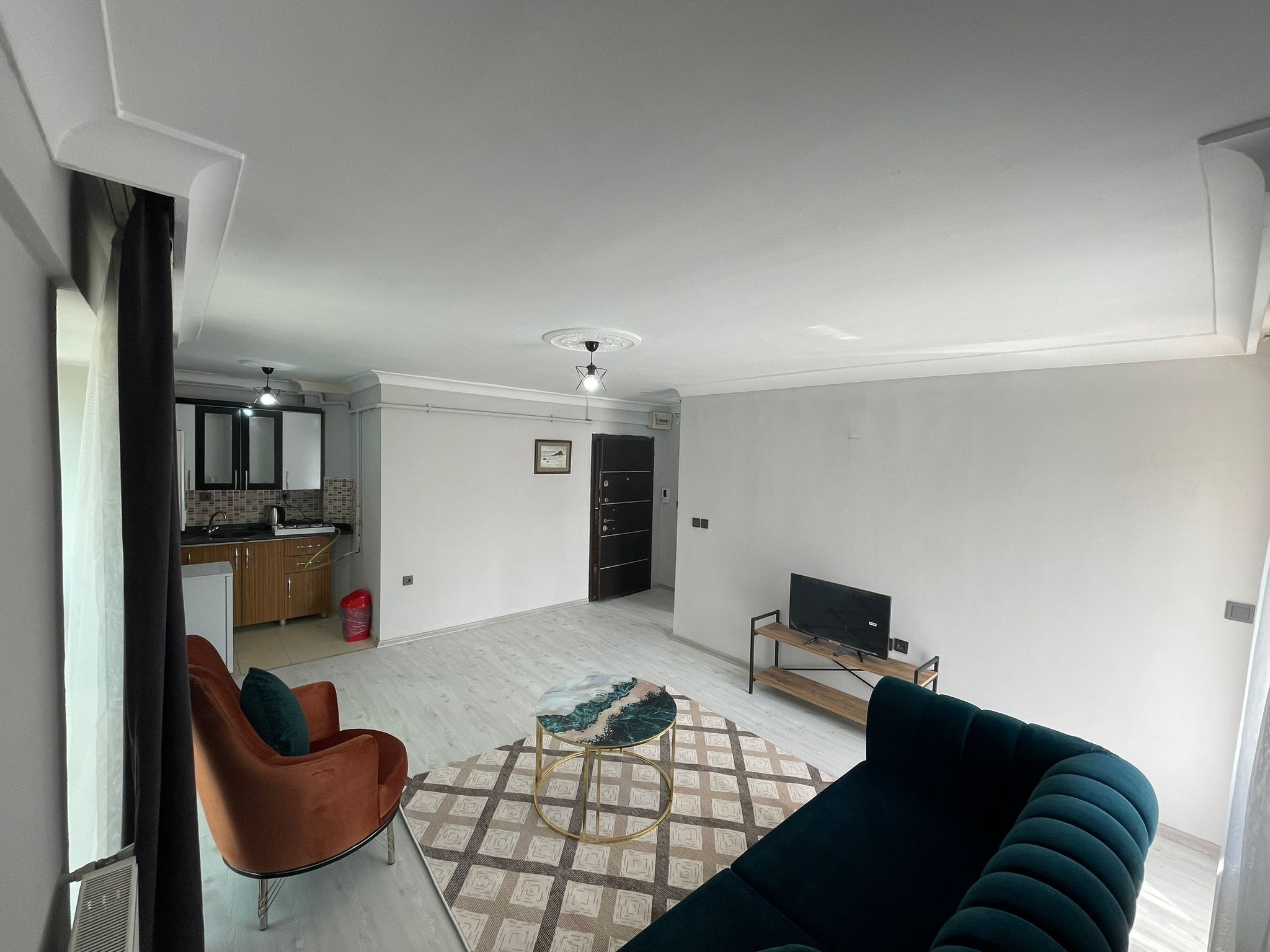 Un salon moderne avec un canapé, une table basse et un téléviseur. On aperçoit à l’arrière-plan un coin cuisine avec des placards et un évier.