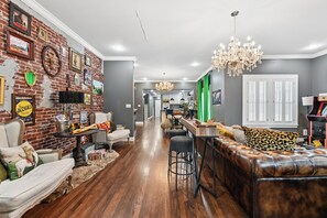 A living room with a brick wall, a chandelier, a leather sofa, and a dining area with a bar.