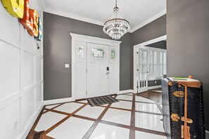 A hallway with a checkered floor, a chandelier, and a white door with a window.
