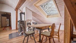 A cozy attic room with a wooden table and chairs, a skylight, and a modern fireplace. - Neu Renovierte Ferienwohnung in Zentraler Ruhiger Lage (Lenggries)