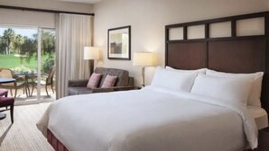 A hotel room with a large bed, a desk with a chair, a sofa, and a view of a golf course through the window. - Excellent retreat near Coachella Valley festival (Palm Desert)