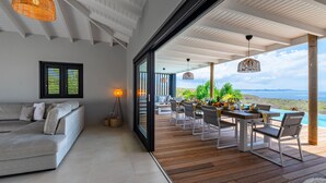 Una sala de estar moderna con un sofá, un comedor con una mesa dispuesta para dos personas y vista al océano.