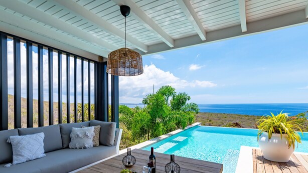 Un espacio exterior moderno con piscina, un sofá y una mesa con frutas y copas de vino.
