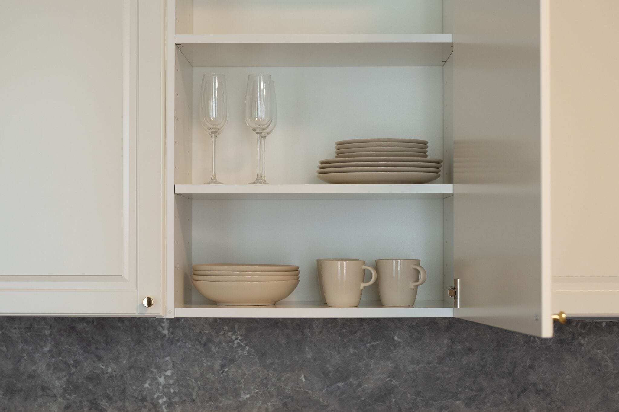 A kitchen cabinet with shelves containing bowls, cups, and wine glasses.
