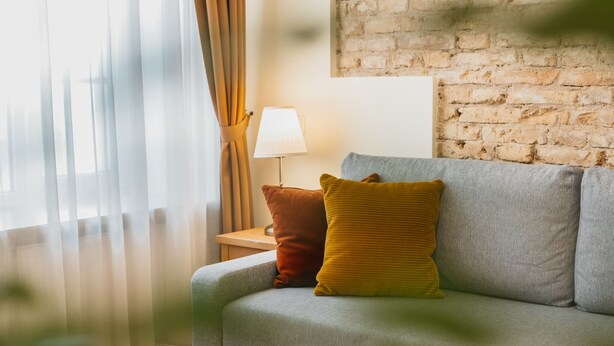 Una sala de estar con un sofá gris, una lámpara y una pared de ladrillo.