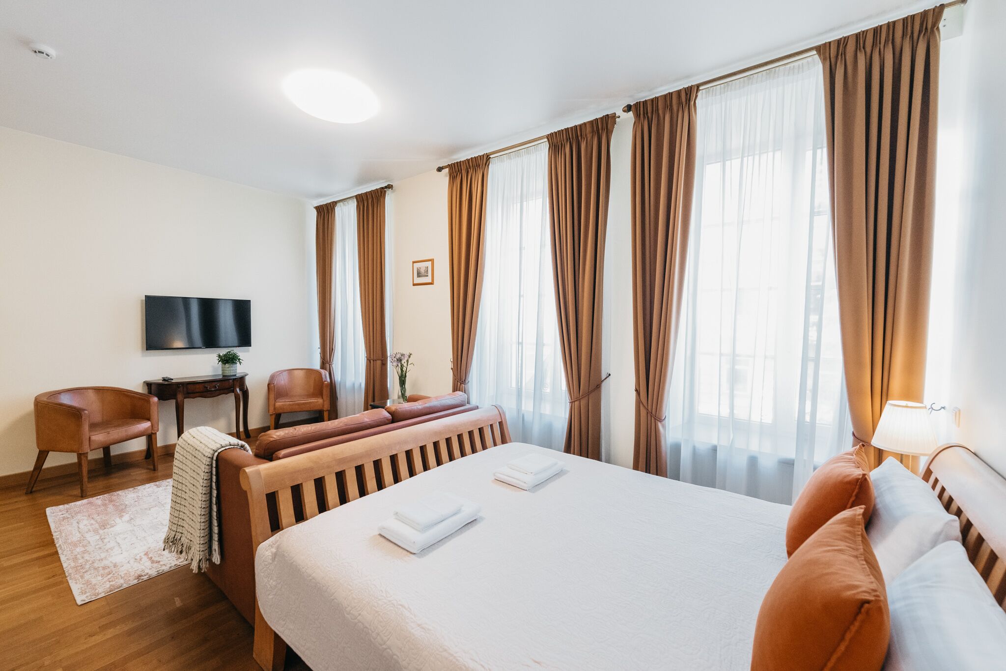A hotel room with a bed, two chairs, a TV, and a desk.