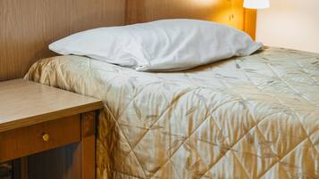 Una cama bien hecha con un edredón acolchado, una mesita de noche con cajón y una lámpara de pared.
