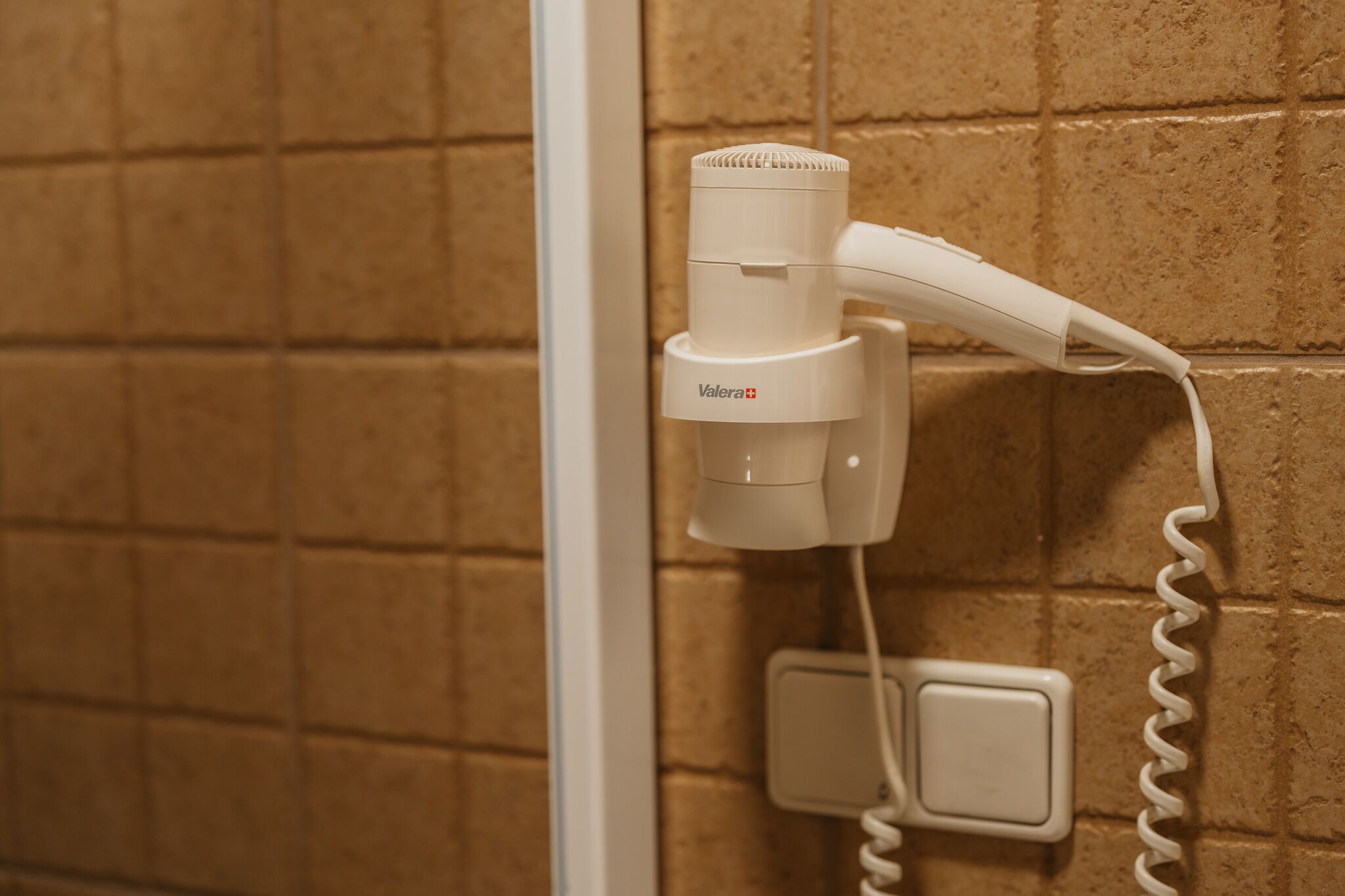 Un secador de pelo sujeto a una pared con azulejos, conectado a un enchufe.