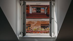 Una ventana con vistas a un edificio de techos rojos y un balcón con plantas.