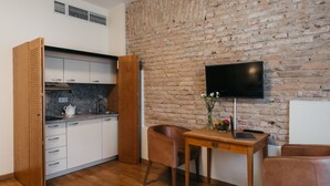 Una cocina compacta con armarios blancos, una puerta de madera y un televisor de pantalla plana montado en una pared de ladrillo.
