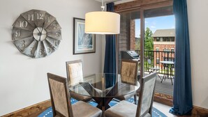 Un comedor con una mesa redonda de vidrio, cuatro sillas, un reloj de pared y una ventana con cortinas.