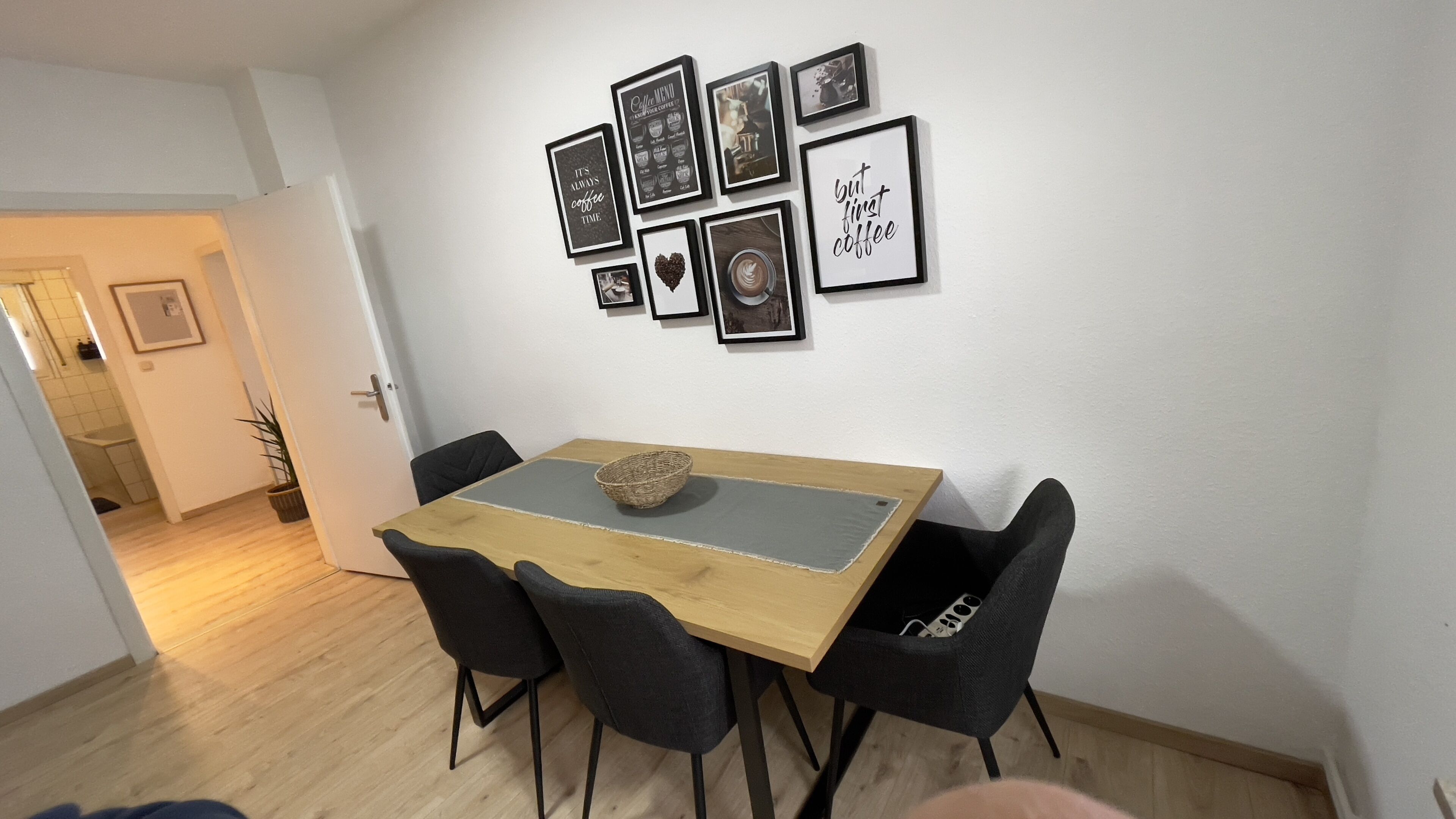 Ein Essbereich mit einem Holztisch und schwarzen Stühlen, einer Wand mit gerahmten Bildern und einer Tür zu einem anderen Raum.