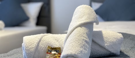 A neatly folded white towel on a striped bedspread with a pillow and a small packet of Karibd.