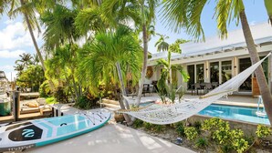 A pool area with a hammock, palm trees, and a poolside lounge. - Waterfront Oasis - Saltwater Pool - Kayaks - Minutes to Fort Lauderdale Beach! (Fort Lauderdale)