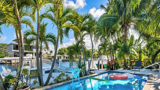 A swimming pool surrounded by palm trees, with a view of boats and a dock in the background. - Waterfront Oasis - Saltwater Pool - Kayaks - Minutes to Fort Lauderdale Beach! (Fort Lauderdale)