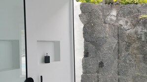 Ein modernes Badezimmer mit Steinwand, schwarzem Duschhandstück und einer kleinen schwarzen Flasche auf einem Regal.
