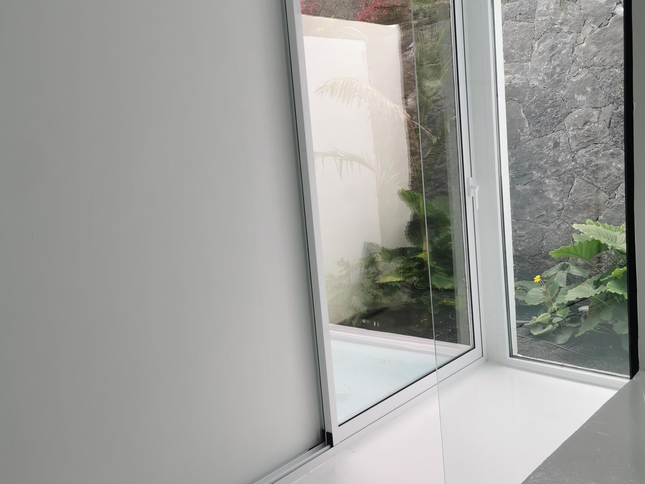 A window with a view of a stone wall and some greenery outside.