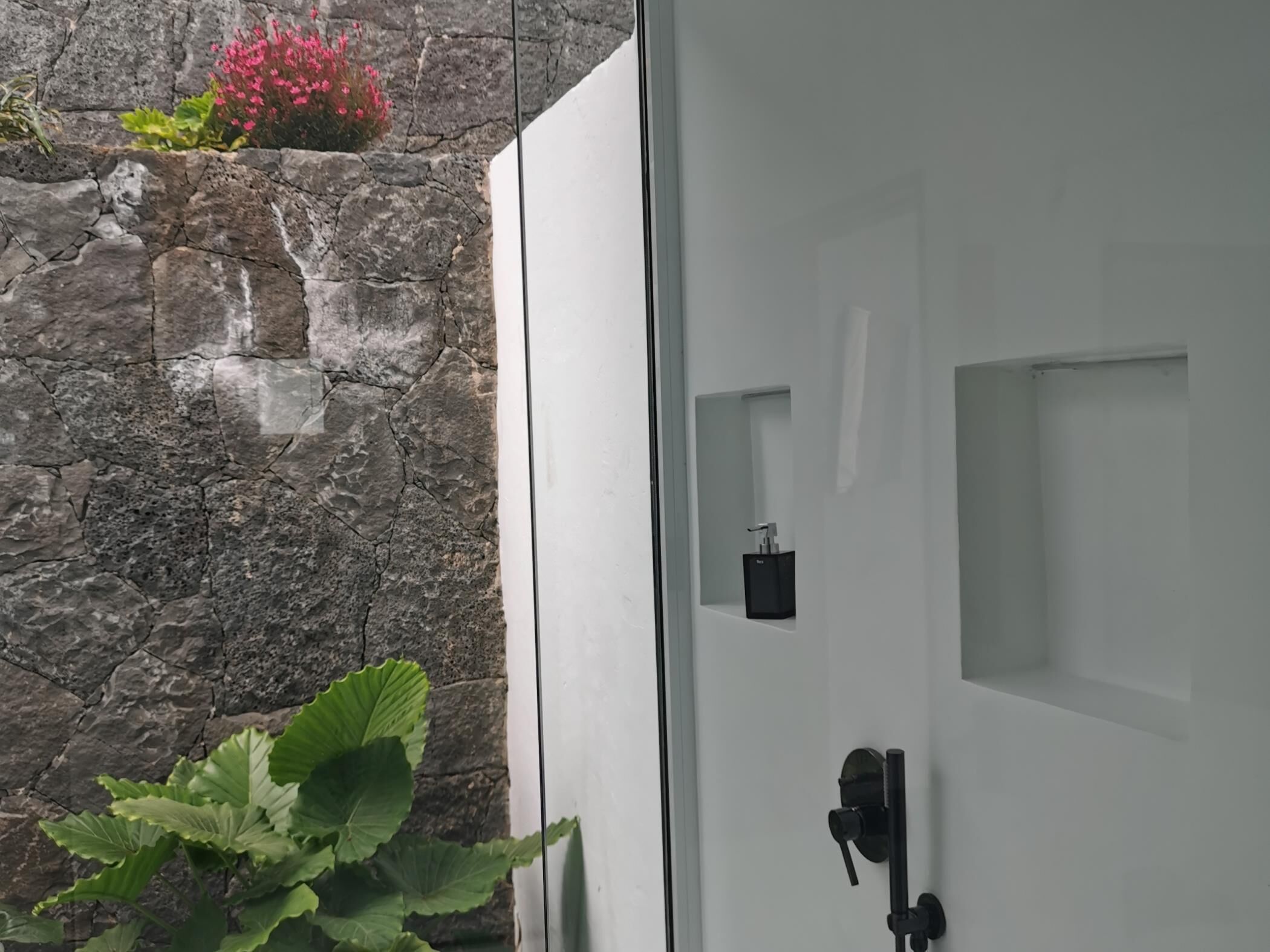 Un baño con pared de piedra, una puerta blanca y un grifo negro.
