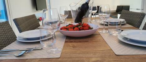 A dining table set with plates, glasses, cutlery, and a bowl of strawberries.