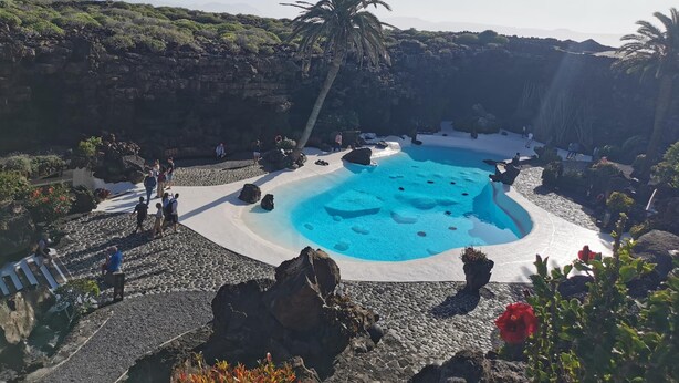 A pool surrounded by rocky terrain and greenery, with people around it.