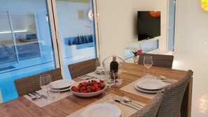 A dining area with a wooden table set for four, including plates, cutlery, and a bowl of strawberries.