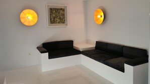 A modern living room with a black sectional sofa, a white accent wall, and two wall-mounted lamps.