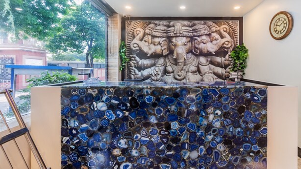 A reception area with a mosaic counter, a wall mural of an elephant deity, and a clock on the wall. - Treebo The Royal Taj (Agra)