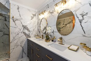 Bathroom features a large mirror, two sinks, and a glass shower enclosure.