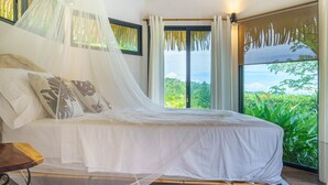 A bed with a canopy, a view of greenery outside, and a window with curtains. - Experience the Pure Life in the Private Jungle Paradise of Ojochal  (Provincia de Puntarenas)