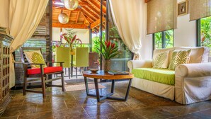 A cozy living area with a sofa, a round wooden coffee table, and a chair with a red cushion. - Experience the Pure Life in the Private Jungle Paradise of Ojochal  (Provincia de Puntarenas)